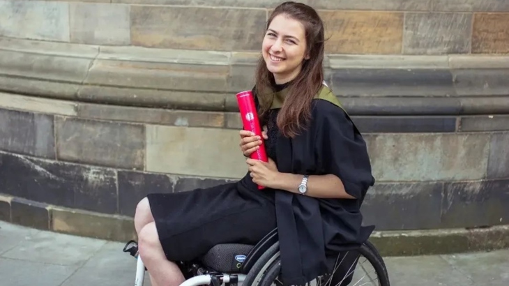 a woman in a wheelchair holding a university diploma