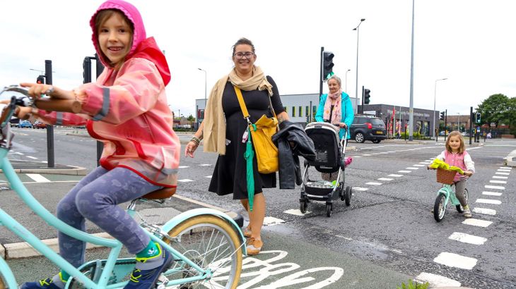 2 adults walking and 2 small children cycling across a road.