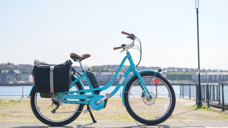 A parked blue e-bike standing at Barry waterfront on a sunny day, with Barry Island in the background.