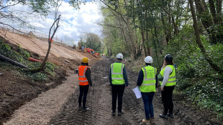 A Group Of People In Safety Vests And Helmets On A Dirt Road