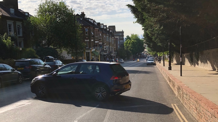 a car beside a narrow pavement on a busy road outside a school